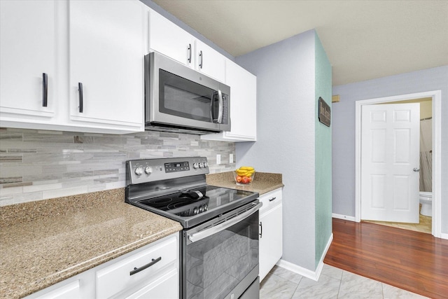 kitchen featuring light stone counters, tasteful backsplash, white cabinetry, stainless steel appliances, and baseboards