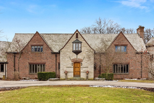 english style home with stone siding, brick siding, a chimney, and a front lawn