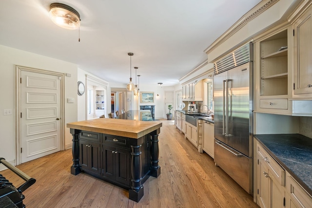 kitchen with butcher block counters, light wood-style floors, stainless steel built in fridge, a sink, and dark cabinets