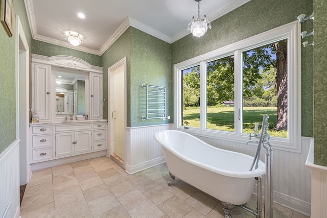 full bath with a wainscoted wall, an inviting chandelier, ornamental molding, vanity, and a freestanding tub