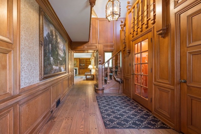 corridor featuring stairway, wood-type flooring, an inviting chandelier, and a decorative wall