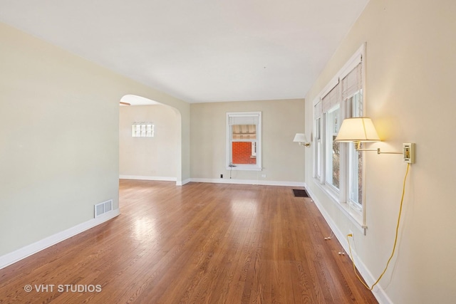 interior space with arched walkways, visible vents, baseboards, and wood finished floors