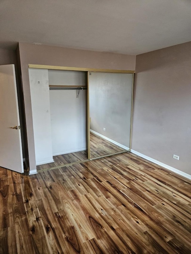 unfurnished bedroom featuring a closet, wood finished floors, and baseboards