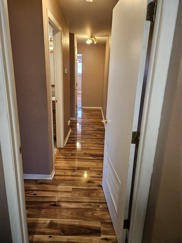 corridor with dark wood-type flooring, visible vents, and baseboards