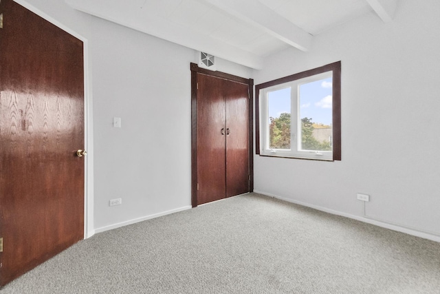 unfurnished bedroom featuring carpet, a closet, baseboards, and beamed ceiling