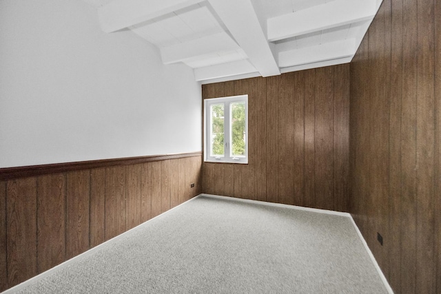 carpeted empty room featuring wooden walls, beam ceiling, and wainscoting