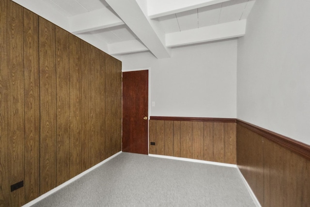 carpeted spare room featuring wood walls, beamed ceiling, and wainscoting