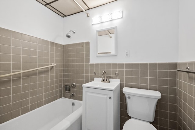 bathroom with toilet, a wainscoted wall, bathing tub / shower combination, vanity, and tile walls