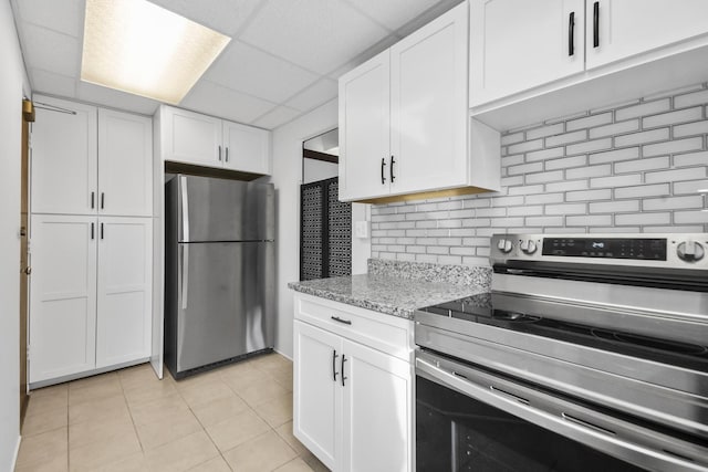 kitchen with light tile patterned floors, light stone counters, stainless steel appliances, a paneled ceiling, and white cabinetry