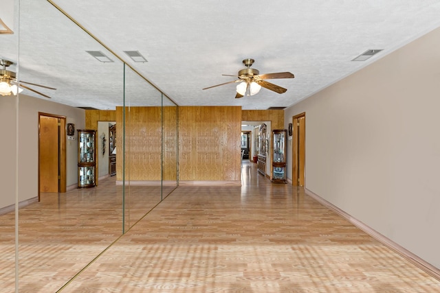 spare room featuring visible vents, ceiling fan, wooden walls, and a textured ceiling