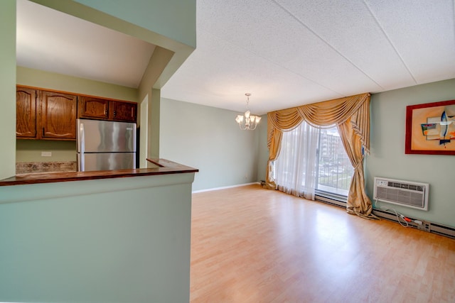 kitchen with freestanding refrigerator, a peninsula, an AC wall unit, light wood-type flooring, and a notable chandelier