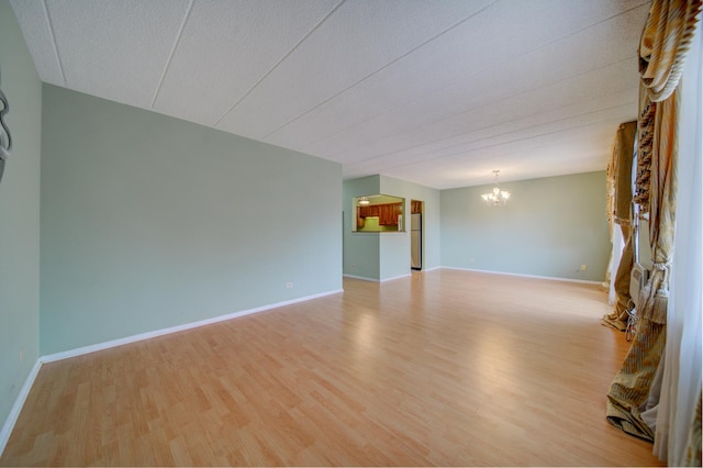 empty room with baseboards, a textured ceiling, light wood-type flooring, and a notable chandelier