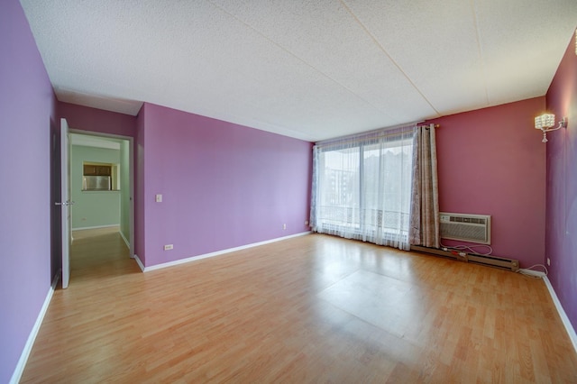 spare room featuring baseboards, a wall unit AC, a baseboard radiator, and light wood-style floors