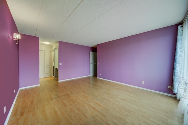 empty room with a textured ceiling, light wood-type flooring, and baseboards