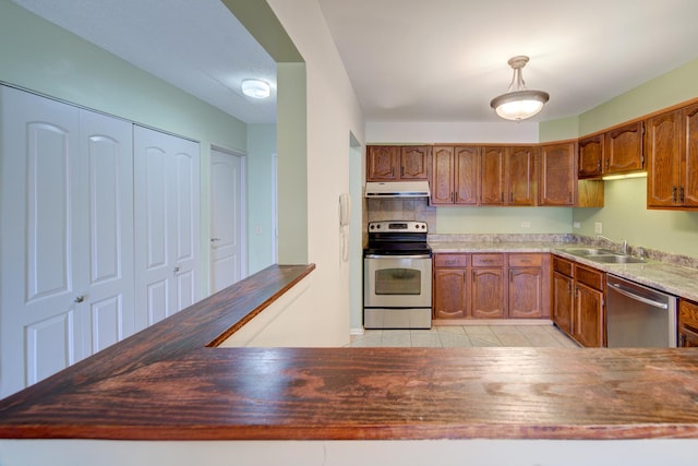 kitchen featuring brown cabinetry, stainless steel appliances, under cabinet range hood, a sink, and light tile patterned flooring