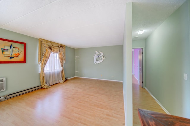 empty room featuring a baseboard heating unit, baseboards, and light wood finished floors