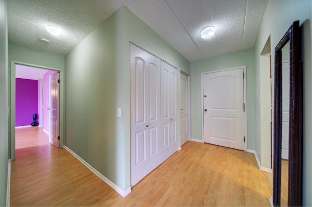 corridor featuring light wood-type flooring, baseboards, and a textured ceiling