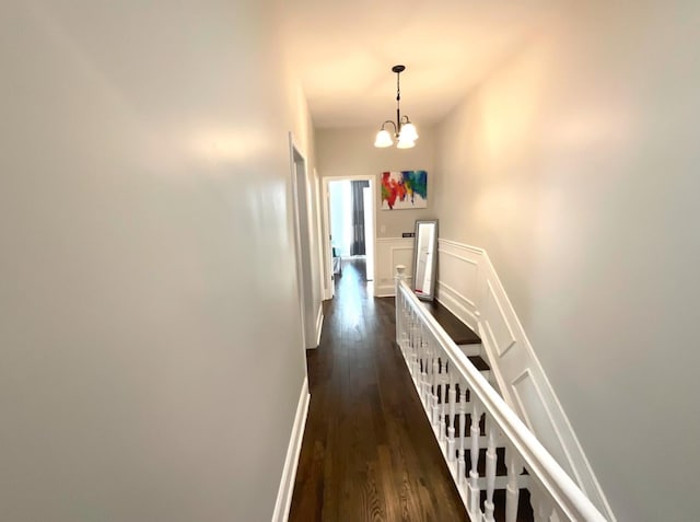 hallway featuring a decorative wall, an upstairs landing, baseboards, dark wood finished floors, and an inviting chandelier