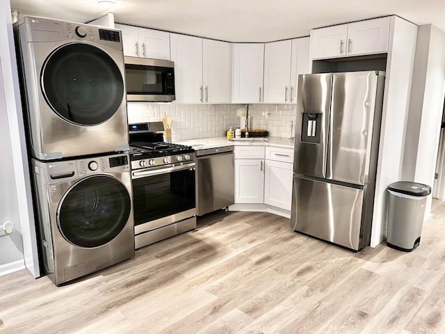 kitchen with stainless steel appliances, tasteful backsplash, stacked washing maching and dryer, and light wood-style floors