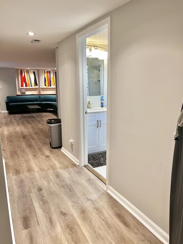 hall featuring a sink, wood finished floors, visible vents, and baseboards