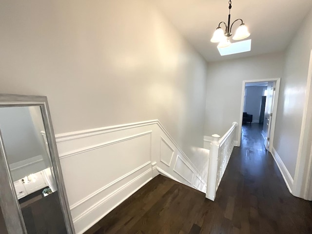 corridor featuring a wainscoted wall, a notable chandelier, a decorative wall, dark wood-type flooring, and an upstairs landing