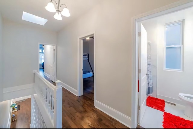 corridor with a skylight, baseboards, visible vents, wood finished floors, and an upstairs landing