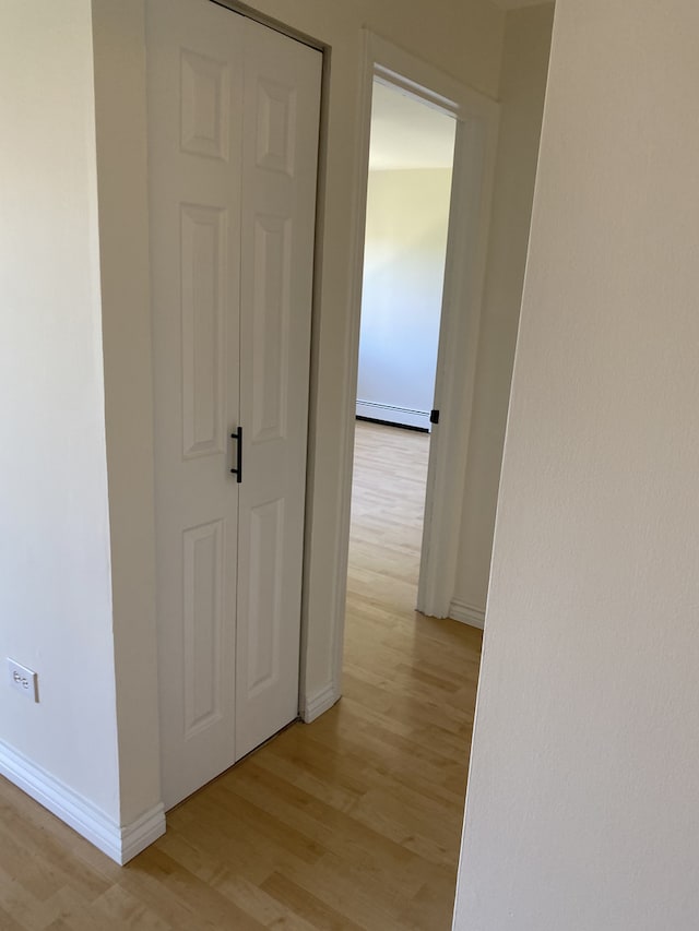 hallway featuring light wood finished floors, baseboards, and baseboard heating