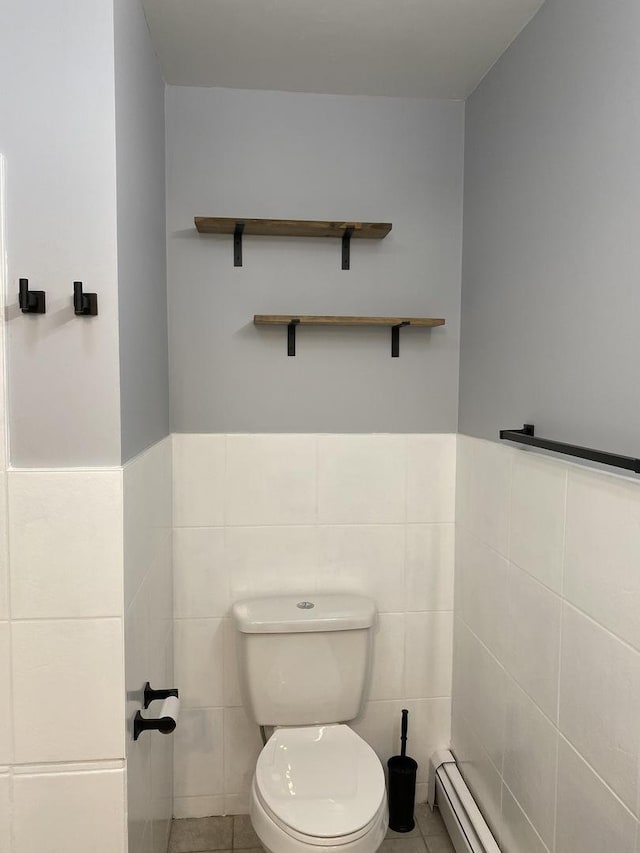 half bath with toilet, a wainscoted wall, tile patterned floors, a baseboard heating unit, and tile walls