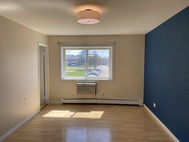 unfurnished room featuring baseboard heating, a wall mounted air conditioner, light wood-style flooring, and baseboards