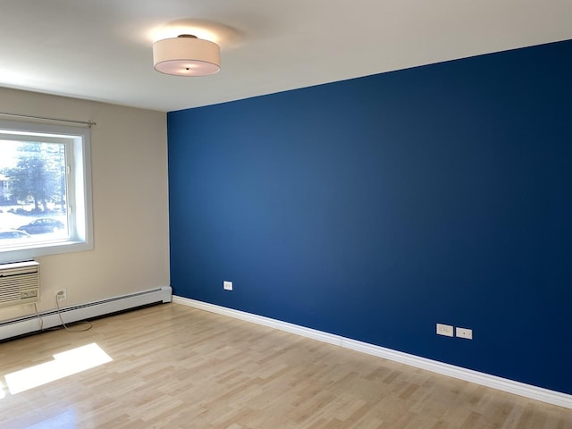 spare room with a baseboard heating unit, light wood-type flooring, and baseboards