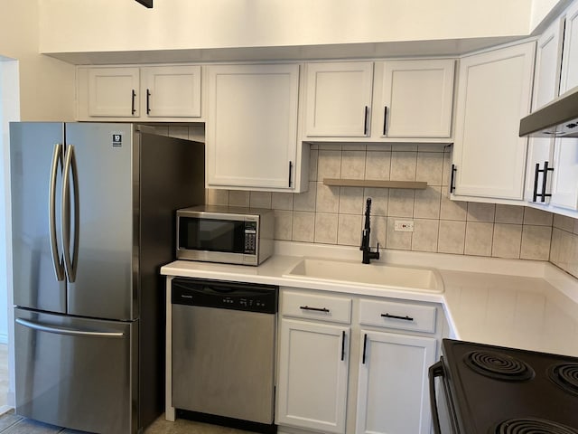 kitchen with appliances with stainless steel finishes, decorative backsplash, a sink, and light countertops