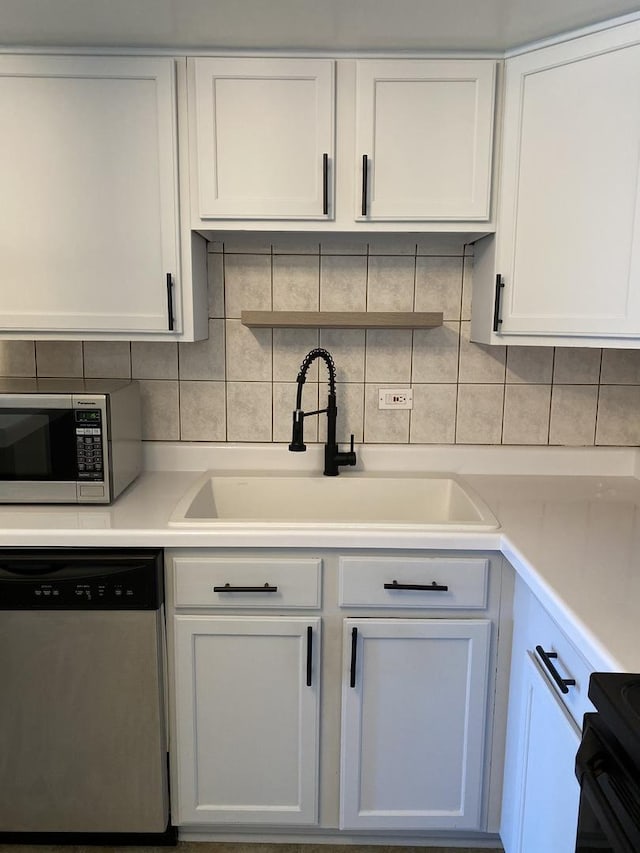 kitchen featuring stainless steel appliances, a sink, white cabinetry, light countertops, and tasteful backsplash