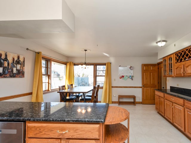 kitchen featuring brown cabinetry, glass insert cabinets, baseboards, and dark stone counters