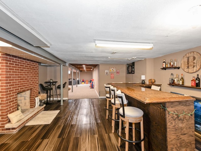 bar featuring a bar, a brick fireplace, dark wood-style floors, and baseboards