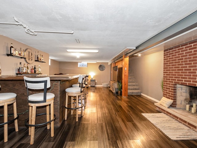 bar featuring dark wood-type flooring, baseboards, stairway, a dry bar, and a fireplace