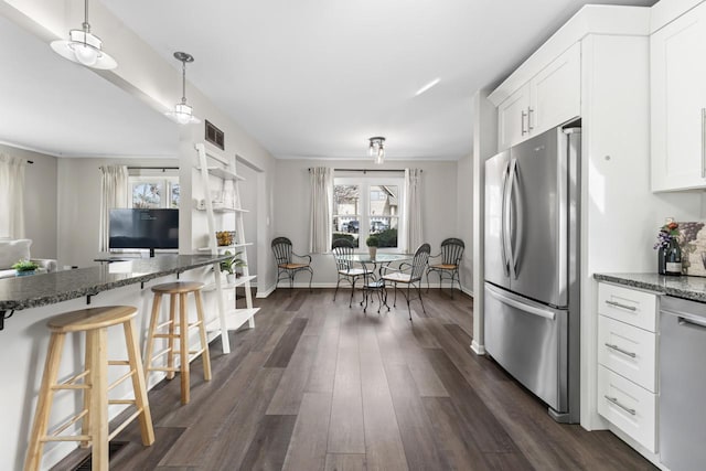 kitchen with visible vents, a kitchen breakfast bar, appliances with stainless steel finishes, dark stone counters, and dark wood finished floors