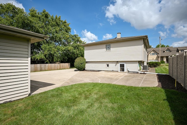 rear view of property featuring a chimney, fence, cooling unit, a yard, and a patio area