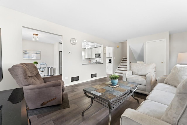 living room featuring dark wood-style flooring, visible vents, stairway, and baseboards