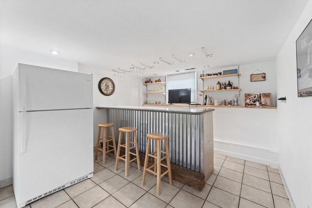 kitchen with light tile patterned floors, a kitchen bar, open shelves, freestanding refrigerator, and baseboards