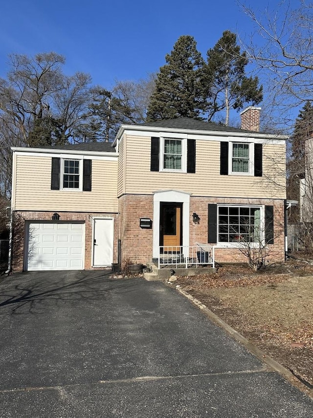 view of front facade featuring a garage, aphalt driveway, a chimney, and brick siding