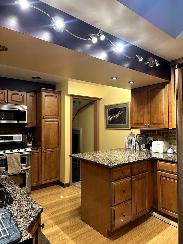 kitchen featuring stainless steel appliances, decorative backsplash, dark stone counters, light wood-type flooring, and a peninsula