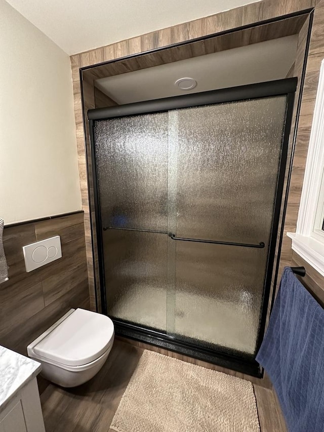 bathroom with tile walls, toilet, a shower stall, vanity, and wood finished floors