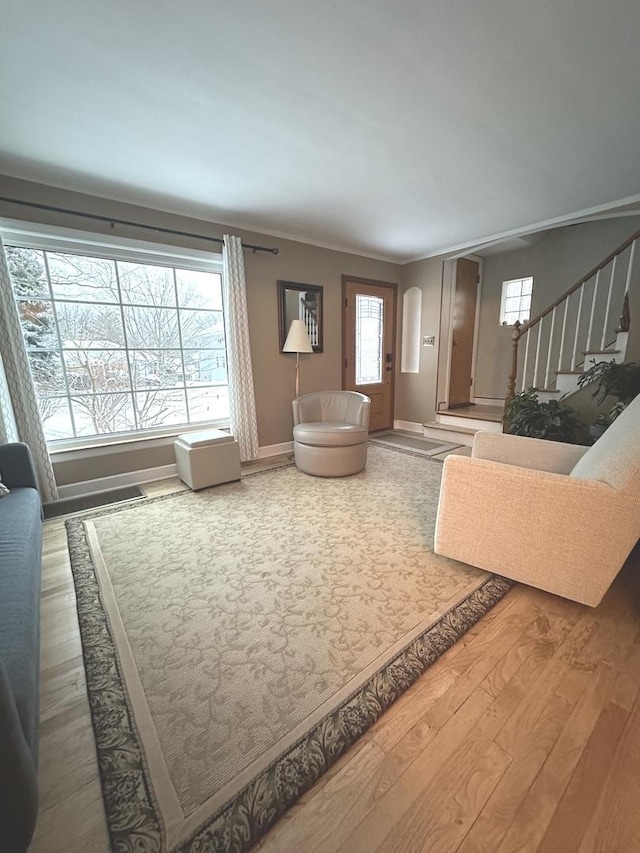 living area featuring stairs, crown molding, baseboards, and wood finished floors