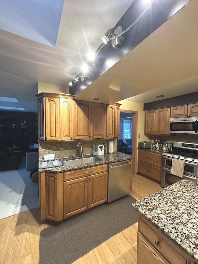 kitchen featuring stainless steel appliances, a sink, backsplash, and dark stone countertops