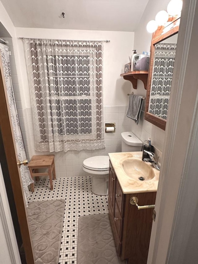 bathroom with tile walls, toilet, wainscoting, vanity, and tile patterned floors