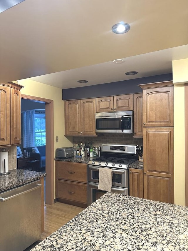 kitchen featuring dark stone counters, appliances with stainless steel finishes, light wood finished floors, and backsplash