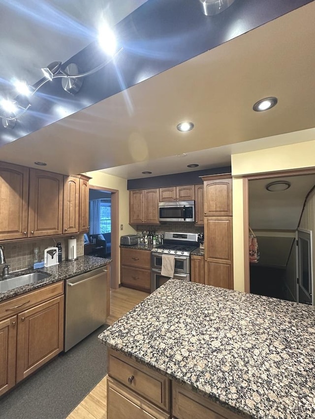 kitchen featuring dark stone counters, appliances with stainless steel finishes, backsplash, and a sink