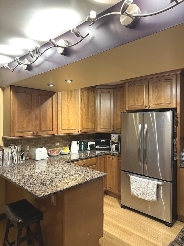 kitchen featuring light wood finished floors, brown cabinetry, freestanding refrigerator, dark stone countertops, and a peninsula