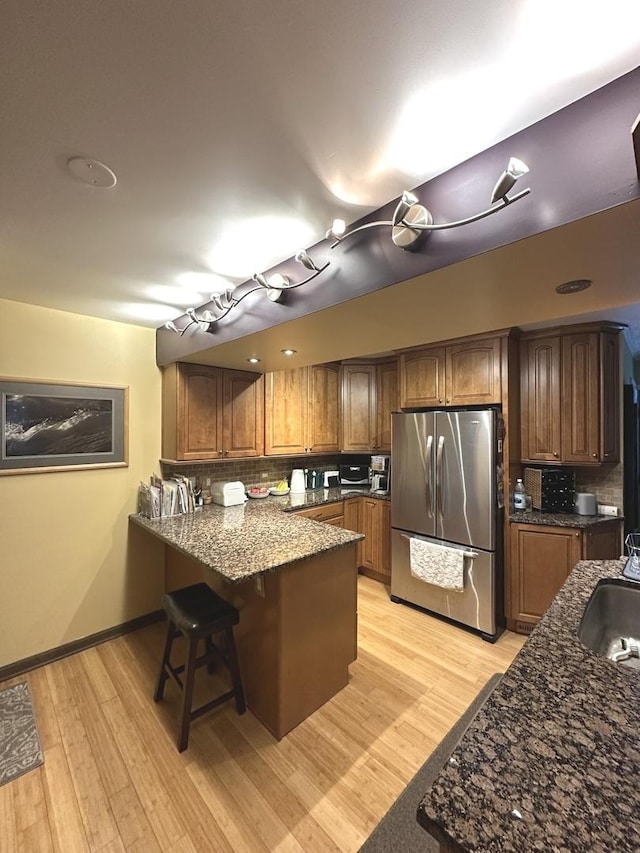 kitchen with light wood-type flooring, freestanding refrigerator, a peninsula, and tasteful backsplash