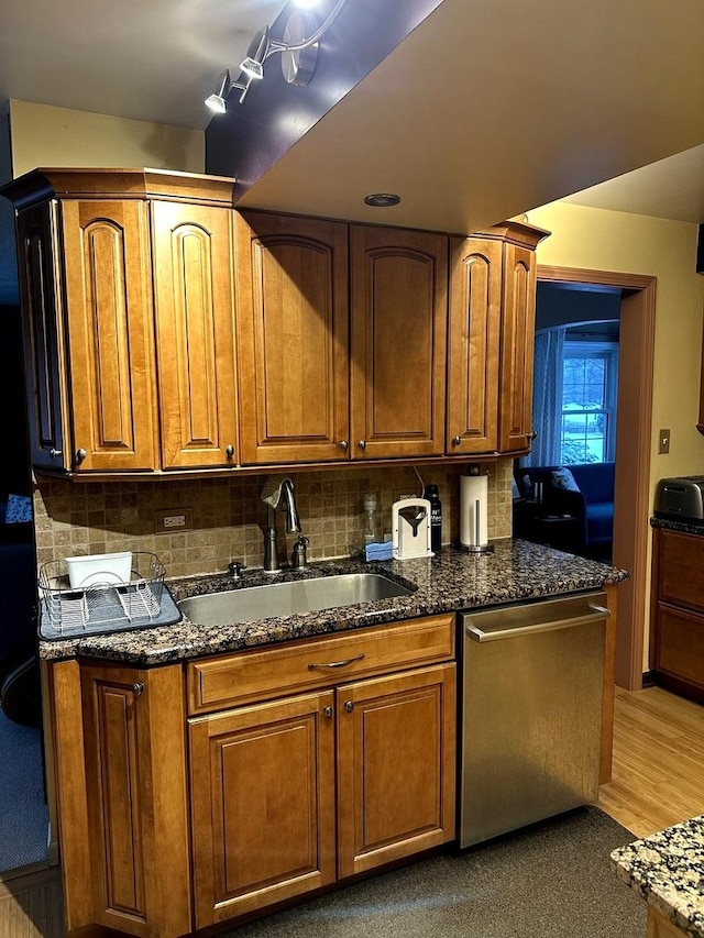 kitchen featuring dark stone counters, a sink, backsplash, dishwasher, and brown cabinetry